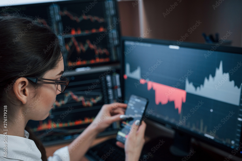 Poster in eyeglasses. woman working online in the office with multiple computer screens in index charts