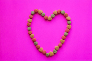 Creative valentines concept photo of Dog food and a heart be lovely on pink background.