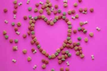 Creative valentines concept photo of Dog food and a heart be lovely on pink background.
