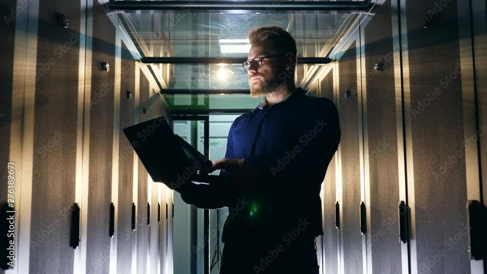 Aufkleber one programmer types on a laptop, checking server room equipment.