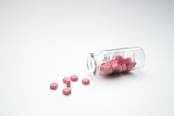 Glass vial with the pink pills on the white table.