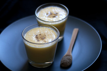 Two glasses of refreshing mango lassi drink, decorated with cardamom. Dark background, selective focus.