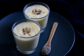 Two glasses of refreshing mango lassi drink, decorated with cardamom. Dark background, selective focus.