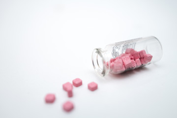 Glass vial with the pink pills on the white table.