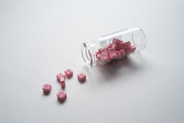 Glass vial with the pink pills on the white table.