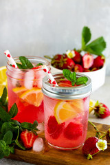 Lemonade with fresh srtawberries, lemons and ice on a light stone or slate table. Free space for your text.