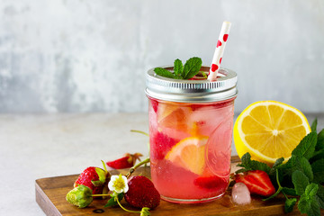 Lemonade with fresh srtawberries, lemons and ice on a light stone or slate table. Free space for your text.