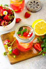 Lemonade with fresh srtawberries, lemons and ice on a light stone or slate table.