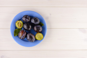 A plate of delicious ripe plum on the white wooden table. Top view, copy space