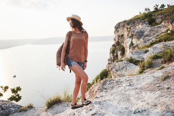 Young girl with backpack enjoying sunset on peak of rocky mountain. Travel lifestyle adventure vacations concept