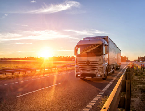 Modern wagon truck transports cargo against the backdrop of a sunset. The concept of truck drivers in the field of freight and logistics, copy space