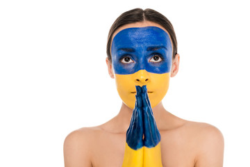 naked young woman with painted Ukrainian flag on skin praying isolated on white