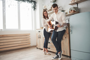 Photo in full growth. Young guitarist playing love song for his girlfriend in the kitchen
