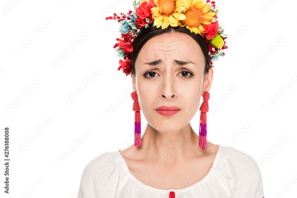 Wall mural upset brunette young woman in national Ukrainian embroidered shirt and floral wreath isolated on white