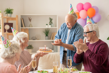Senior friends clapping hands to their friend with birthday cake