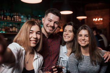 Photo like from the phone. Friends taking selfie in beautiful nightclub. With drinks in the hands
