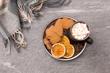 drinks and season concept - cup of hot chocolate with marshmallow, dried orange, heart shaped gingerbread cookies, cinnamon and anise on plate or tray and warm blanket