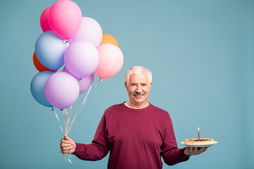 Happy senior man with bunch of balloons and birthday cake