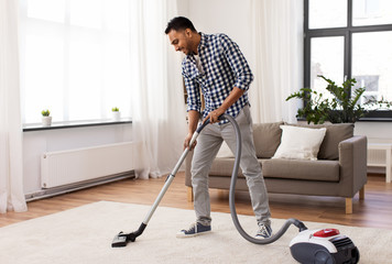 household and cleaning concept - indian man with vacuum cleaner at home