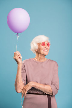 Happy senior female in elegant dress holding balloon