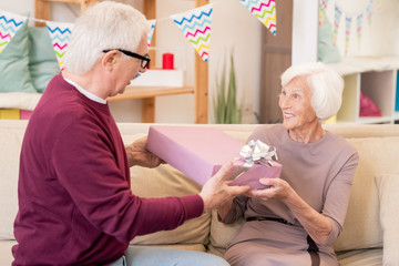 Cheerful senior female taking present from hands of her husband