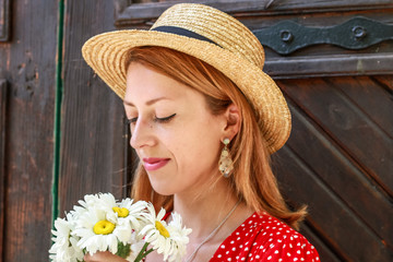 Photosession model with decorations of epoxy resin. Bijouterie. Red dress in peas. Straw hat. Stylish images. Fashion. Summer Trends 2019. Old architecture in the background.