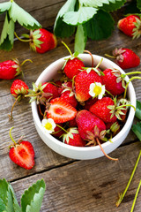 Fresh strawberries in a bowl on a wooden rustic table.