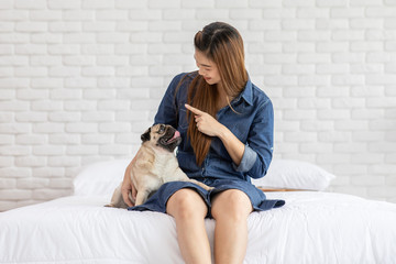 Beautiful Asian young woman playing with her dog and smile with dog pug breed looking in funny and serious face in bedroom feeling so happiness and relaxation,Dog Friendship Concept