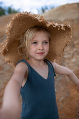 Little cute girl in stylish clothes on a background of rocks. Summer portrait of a little girl in a hat and cotton clothes for a magazine or advertisement