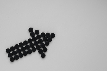 Medical activated carbon in the form of an arrow on a gray background. Top view, copy space.