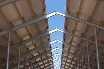 Roof structure consisting of a metal frame, wooden beams and foam insulation against a blue sky....