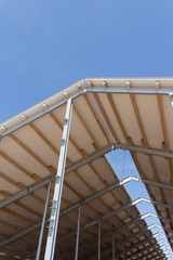 Roof structure consisting of a metal frame, wooden beams and foam insulation against a blue sky. Agricultural constructions. The roof of the new barn.