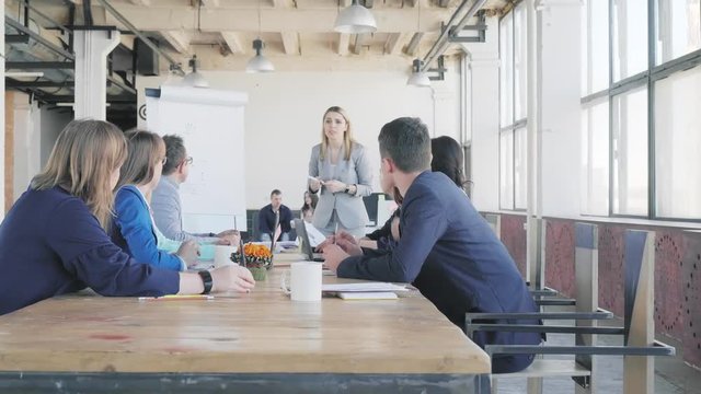 The team leader discusses with colleagues and conducts a presentation using a flipchart, describes business processes. Employees sit at the table. Office life. Coworking. Modern interior in loft style