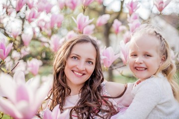 Beautiful young mother and little daughter near a blooming magnolia. Spring. Pink blooms.
