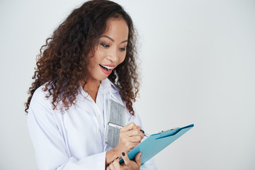 Cheerful excited female physician filling medical history of patient, isolated on white