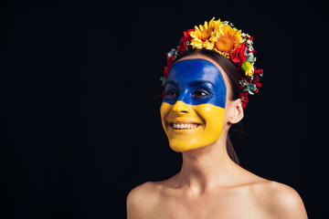happy naked young woman in floral wreath with painted Ukrainian flag on skin isolated on black