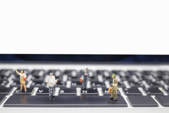 Business, Travel, Technology and information concept. Close up of group of businessman miniature figures with suitcase and newspaper walking and standing on computer laptop keyboard with copy space.