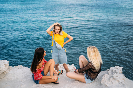 Portrait of three young female friends sitting on the sea shore looking the sea. Multiracial young women in a beach.