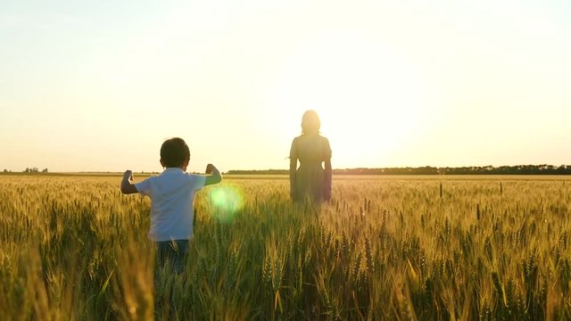 A happy child runs into the arms of his mother over a field of wheat against the backdrop of a sunset.