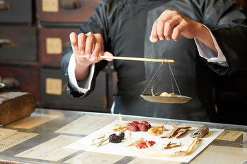 Close-up image of traditional Chinese medicine practitioner using special scales to weight dry...