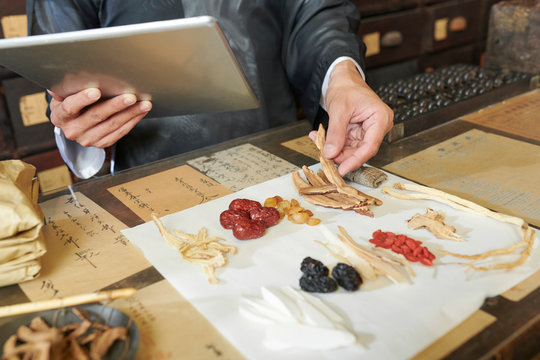 Hands of practitioner putting traditional treatment ingredients on white sheet in front of him