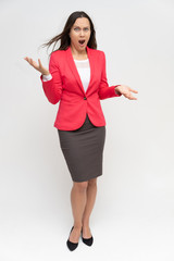 Full-length portrait of a young pretty brunette woman 30 years old in a bright red business suit with beautiful dark hair. Standing on a white background, talking, showing hands, with emotions