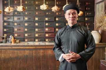 Portrait of smiling mature apothecary owner standing in straditional dress and headwear