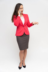 Full-length portrait of a young pretty brunette woman 30 years old in a bright red business suit with beautiful dark hair. Standing on a white background, talking, showing hands, with emotions