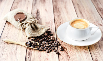 Cup of hot coffee and coffee beans in a wooden scoop and spilling out from a hessian bag on wooden rustic table. Close-up.
