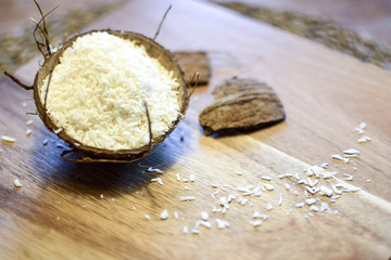Coconut chips in a coconut shell. Tropical still life on a wooden surface.