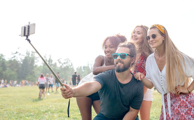 Friends at music festival taking live video to social media using smartphone on selfie stick