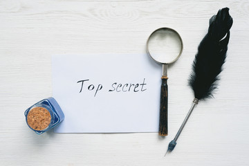 Top secret letter in envelope, magnifying glass and quill pen on a white wooden table flat lay...