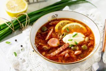 Traditional Russian soup Solyanka with meat, sausages, vegetables, capers, pickles and olives with lemon on wooden table. Rustic style.
