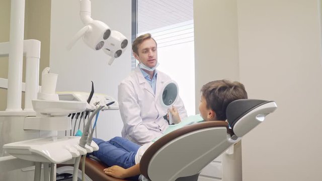 Cheerful little boy and his dentist smiling to the camera. Mature male dentist talking to his little patient after medical examination. Charming kid at dental clinic